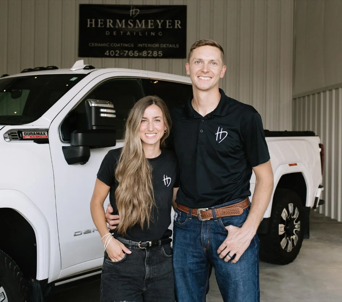 Rusty and Linzie Hermsmeyer, owners of Hermsmeyer Detailing, standing in front of a customer's white GMC Denali in the Central City shop