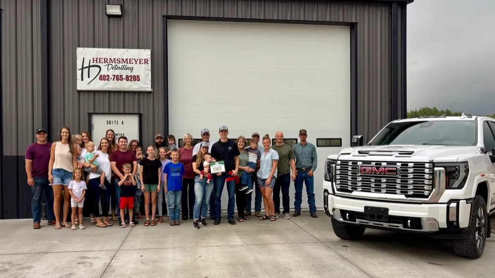 The Hermsmeyer family and friends celebrating outside their Central City detailing shop, with the Hermsmeyer Detailing sign and a customer's GMC Sierra Denali